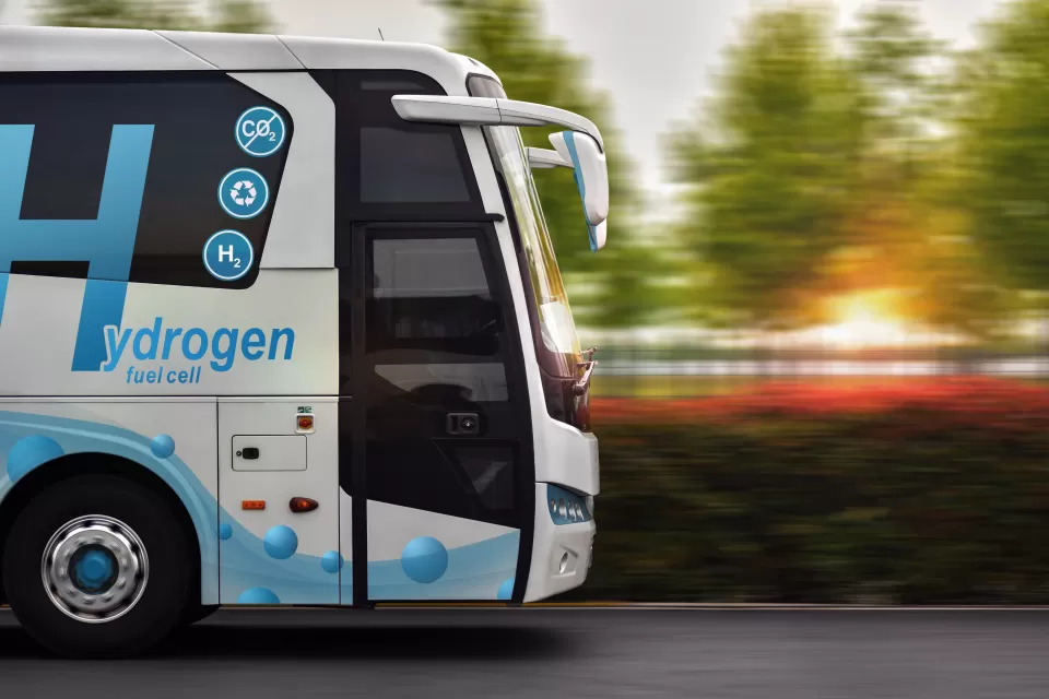 Side view of white bus with blue hydrogen fuel logo driving down the street.